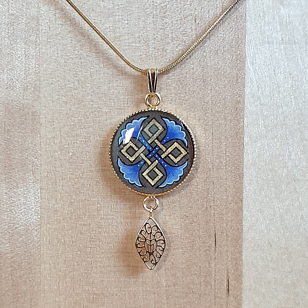 Collier pendentif médaillon doré avec palmettes et entrelacs bleus.