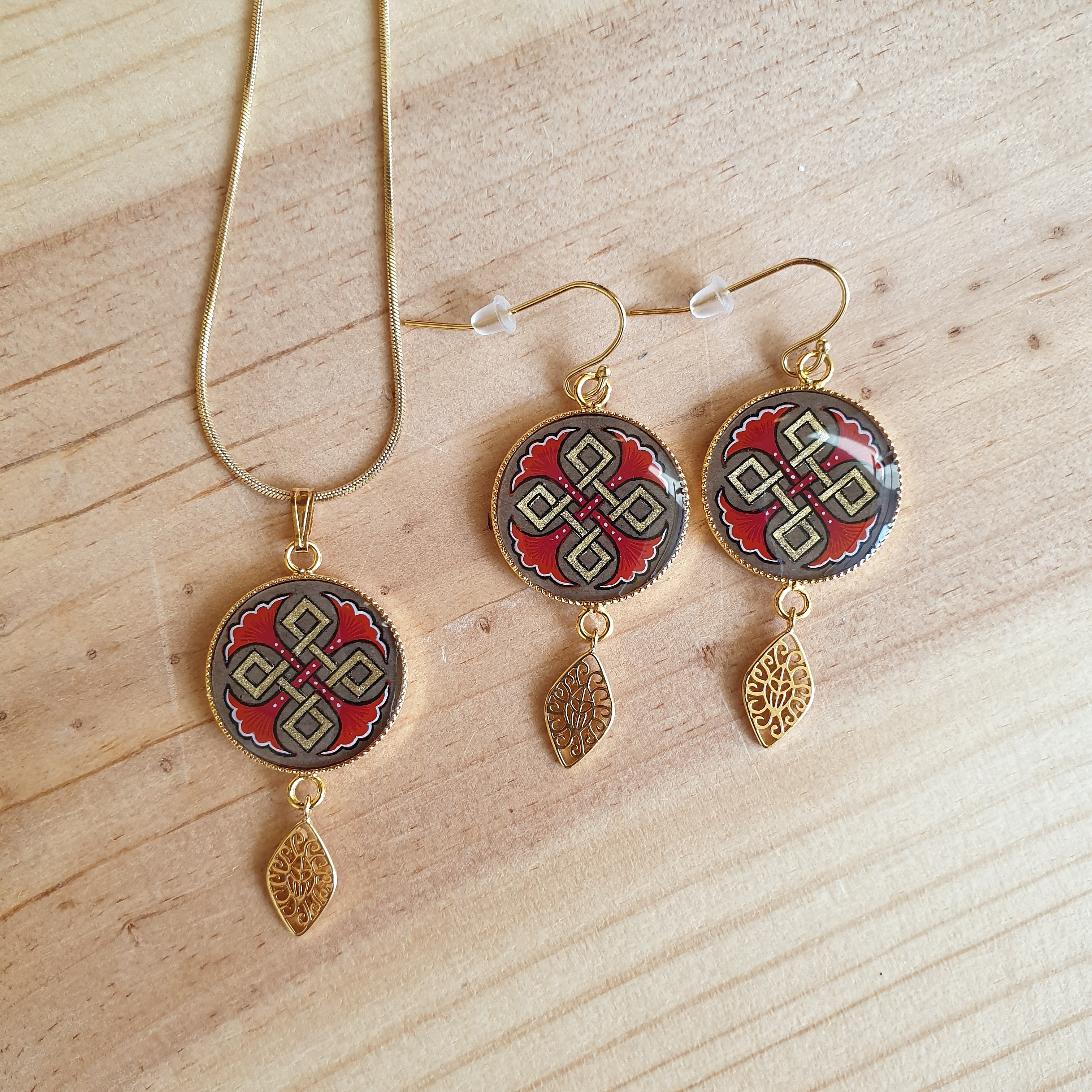 Parure collier et boucles d'oreilles dorés, motifs palmettes rouges.