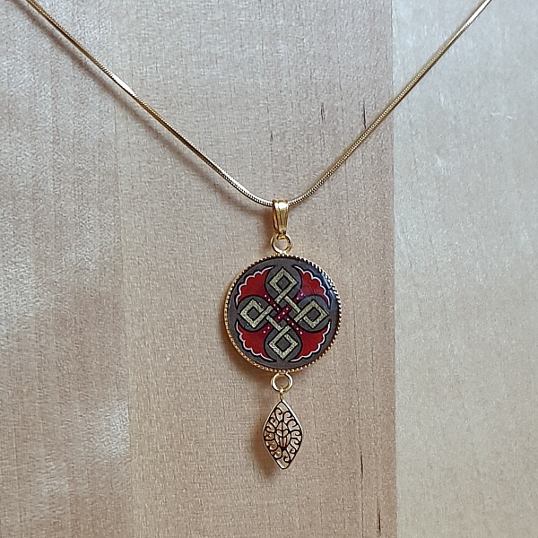 Collier pendentif médaillon doré avec entrelacs rouges et or.