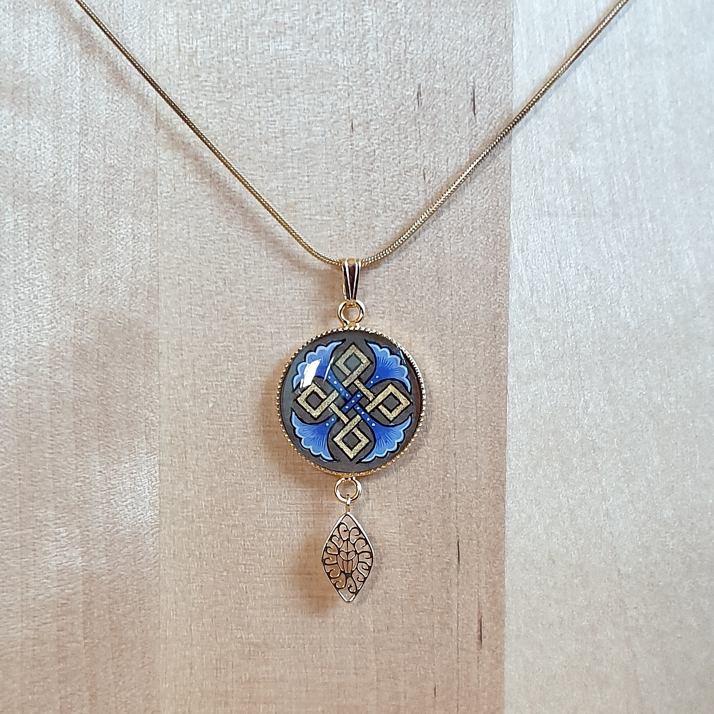 Collier pendentif médaillon doré avec palmettes et entrelacs bleus.